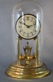 Reloj Alemán, metal dorado con fanal de vidrio, péndulo giratorio. . 31 cm.