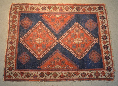 Pequeña alfombra oriental con dos rombos bordó, sobre fondo azul. 126 x 101 cm.