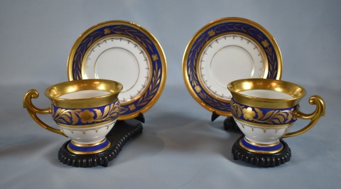 Dos tazas con platos, porcelana blanca con decoración azul y dorado.