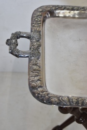 Bandeja de metal plateado con guarda repujada de motivos vegetales, con pie tijera de madera torneada.