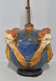 Lámpara de mesa de cerámica con cabezas y guirnaldas. Pequeños deterioros. Con pantalla. Alto vaso: 25 cm.