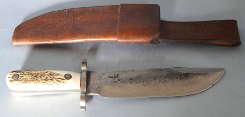 Cuchillo con cabo de asta y hoja de acero. Vaina de cuero. 33 cm de largo.