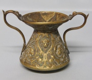 Vaso de bronce, pequeño con asas, con cabezas de leones. Averías, restauro. Alto: 9,5 cm.